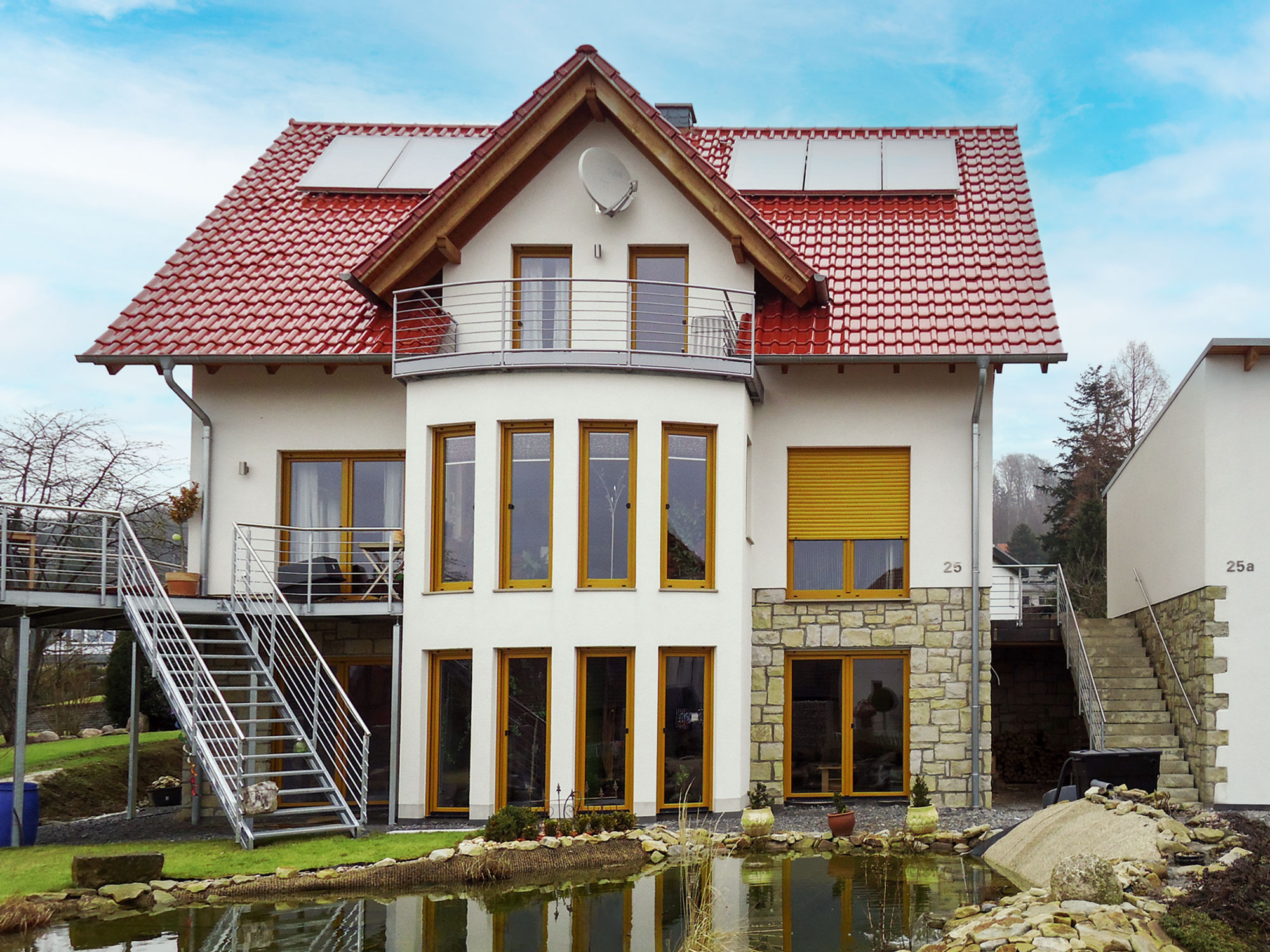 Massiv gebautes Doppelhaus mit Natursteinarbeiten und moderner Architektur Modernes Doppelhaus mit Garage, Natursteinfassade, Balkon und Teich