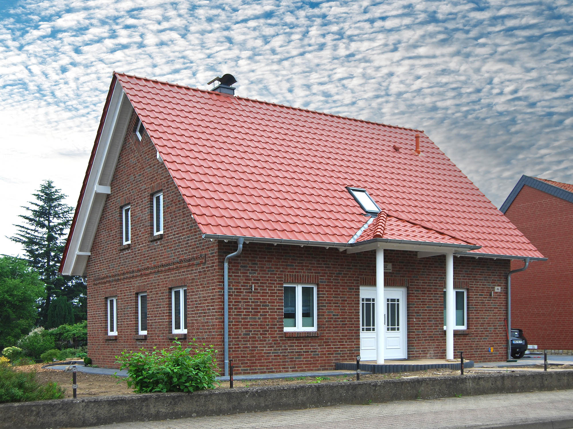 Zweigeschossiges Klinkerhaus mit rotem Satteldach, weißen Fenstern und überdachtem Eingangsbereich.