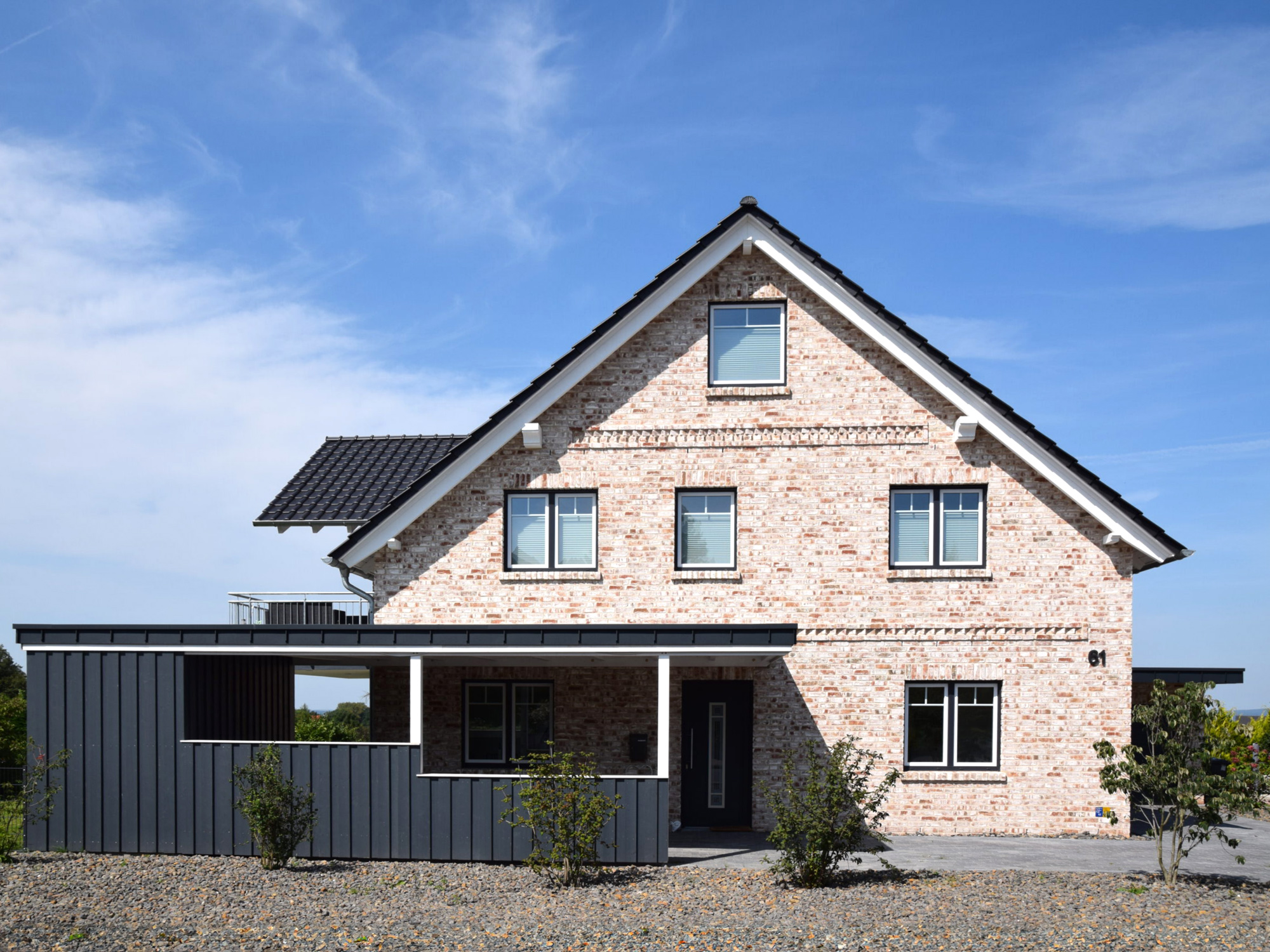 Haus mit heller Klinkerfassade, überdachter Garage, neu gepflastertem Weg und frisch angelegtem Vorgarten mit Kiesfläche.
