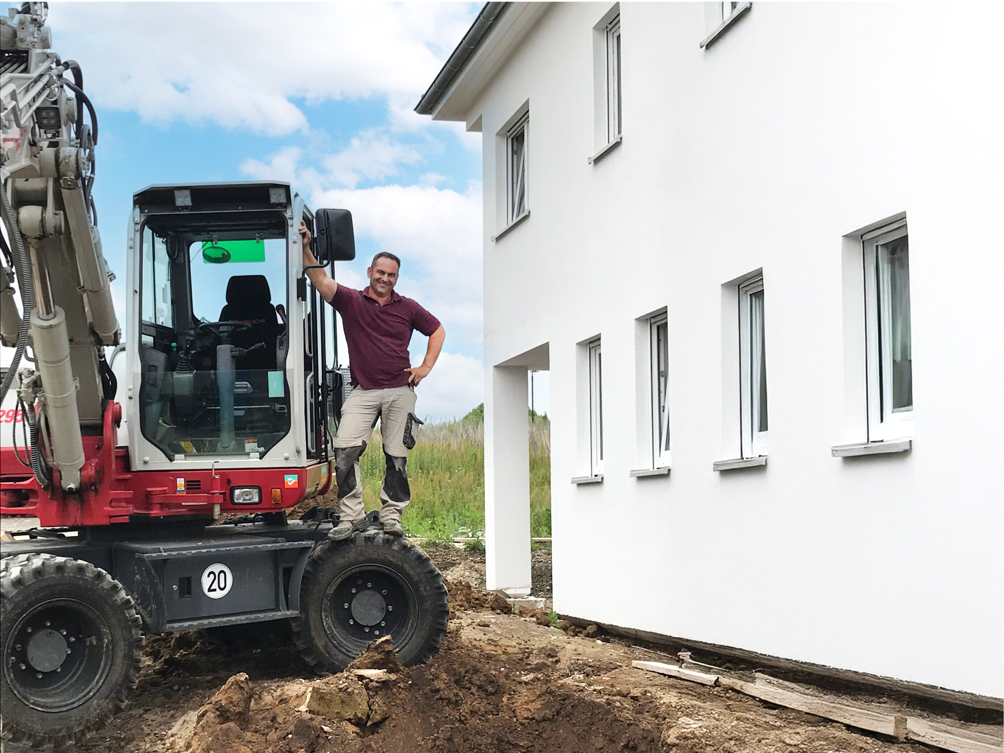 Maurermeister Denis Haase mit Bagger neben einem Wohnhaus auf einer Baustelle Maurermeister Denis Haase steht auf einem Bagger neben einem weißen Haus, im Vordergrund ist eine ausgehobene Baugrube zu sehen.