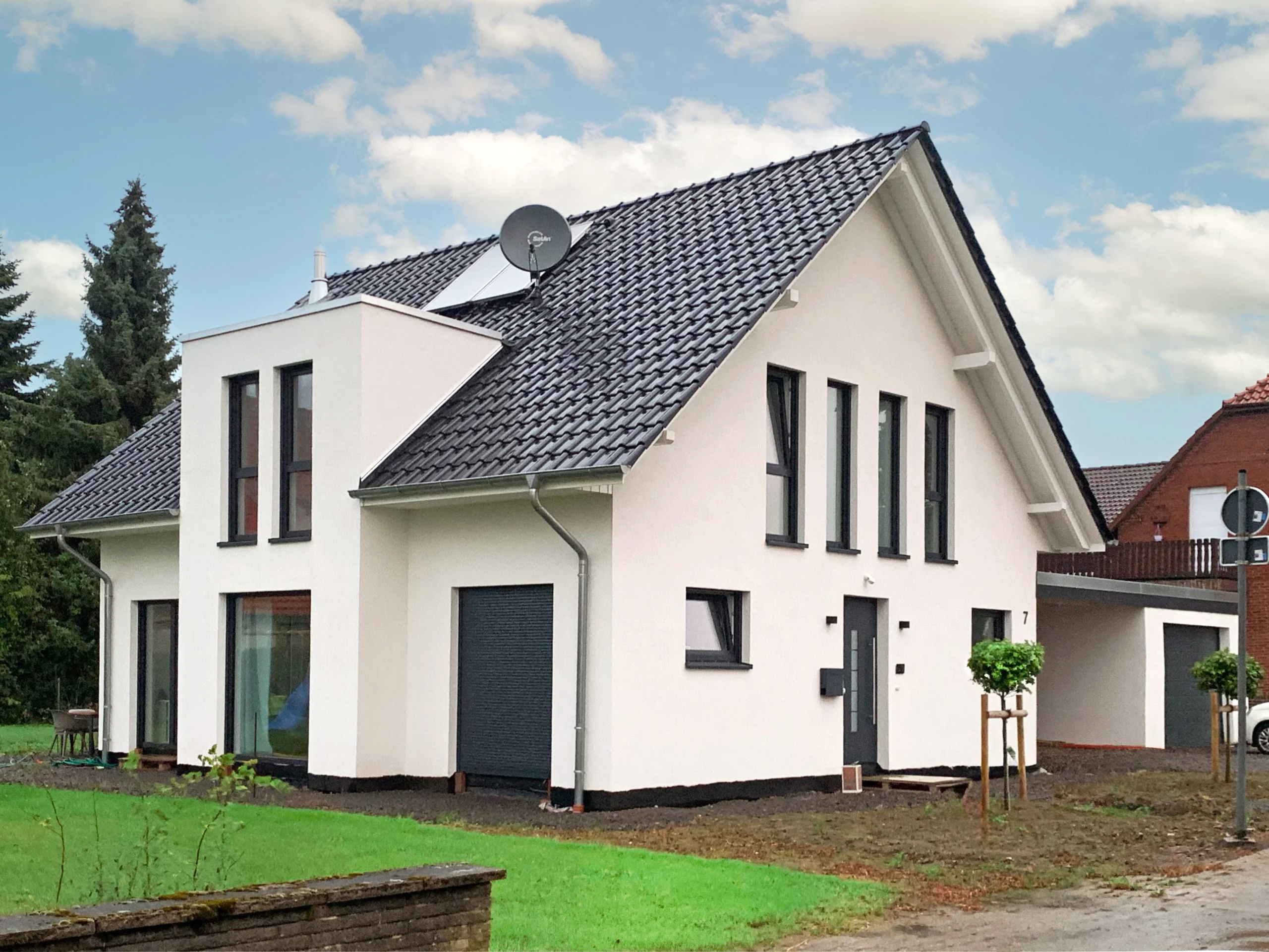 Neubau eines modernen Einfamilienhauses mit Satteldach und Carport Modernes weißes Einfamilienhaus mit Satteldach, großen Fenstern und Carport auf frisch angelegtem Grundstück.